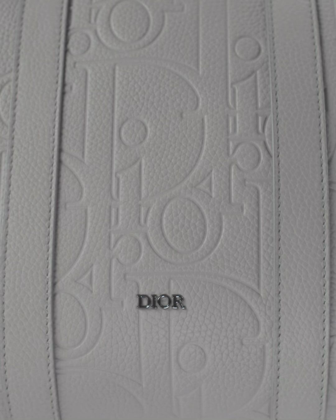 Close-up of a white leather handbag with raised 'Dior' logo pattern and leather straps, showcasing luxury fashion and brand detailing.
