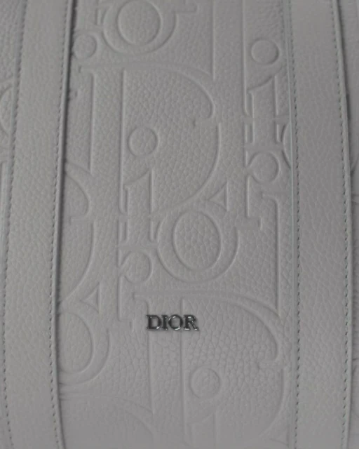 Close-up of a white leather handbag with raised 'Dior' logo pattern and leather straps, showcasing luxury fashion and brand detailing.