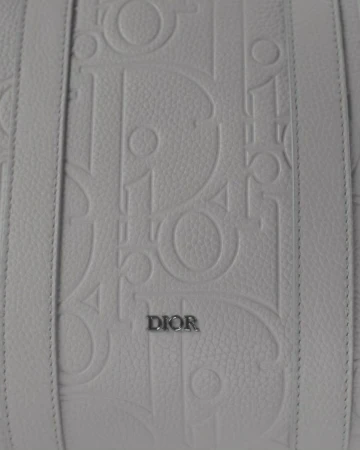 Close-up of a white leather handbag with raised 'Dior' logo pattern and leather straps, showcasing luxury fashion and brand detailing.