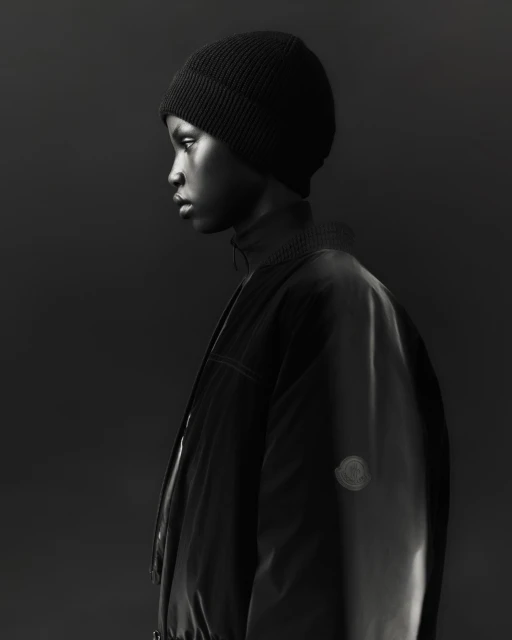 Monochrome portrait of a young adult in black beanie and jacket, captured in a photo studio setting with minimalist lighting.