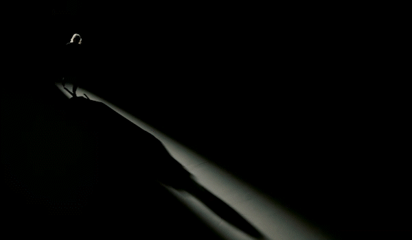 Silhouette of a person standing in a dark room, with a single light source creating a long shadow.
