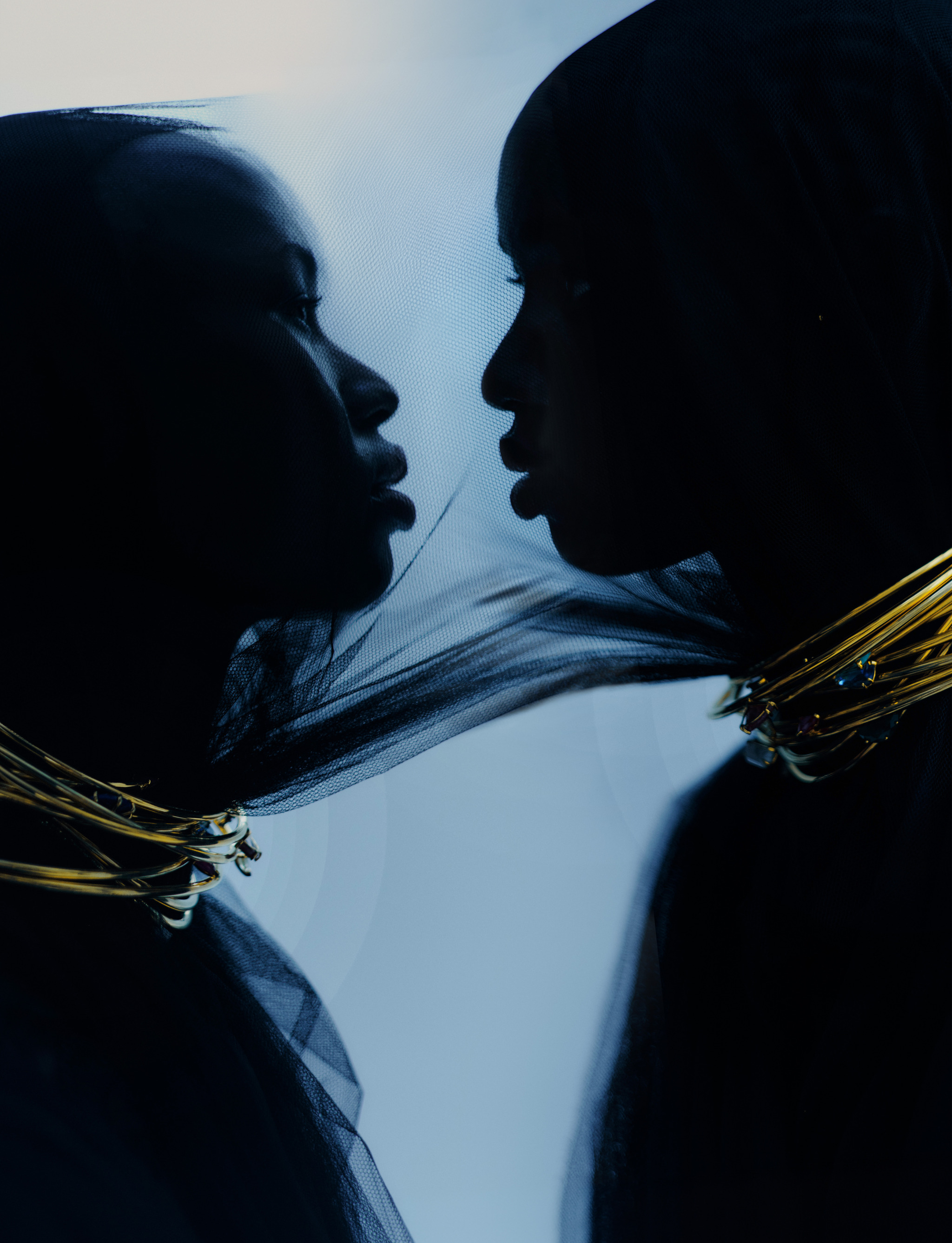Silhouetted profiles of two Black women face each other, adorned with gold necklaces, set against a soft, light blue backdrop.