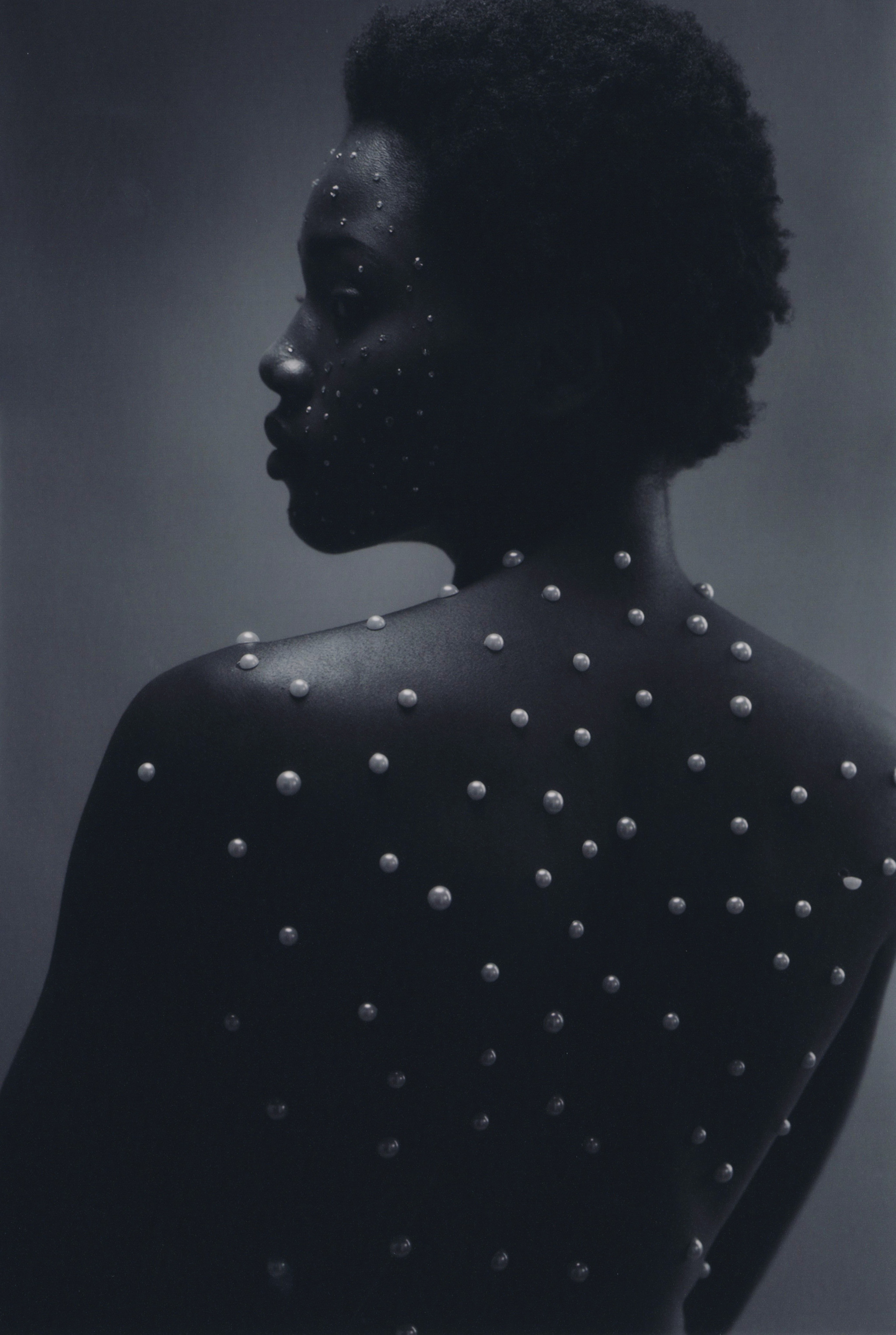 Close-up shot of a bare-backed African-American woman adorned with pearls, presenting a striking contrast against a dark grey background.