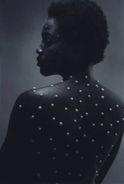 Close-up shot of a bare-backed African-American woman adorned with pearls, presenting a striking contrast against a dark grey background.