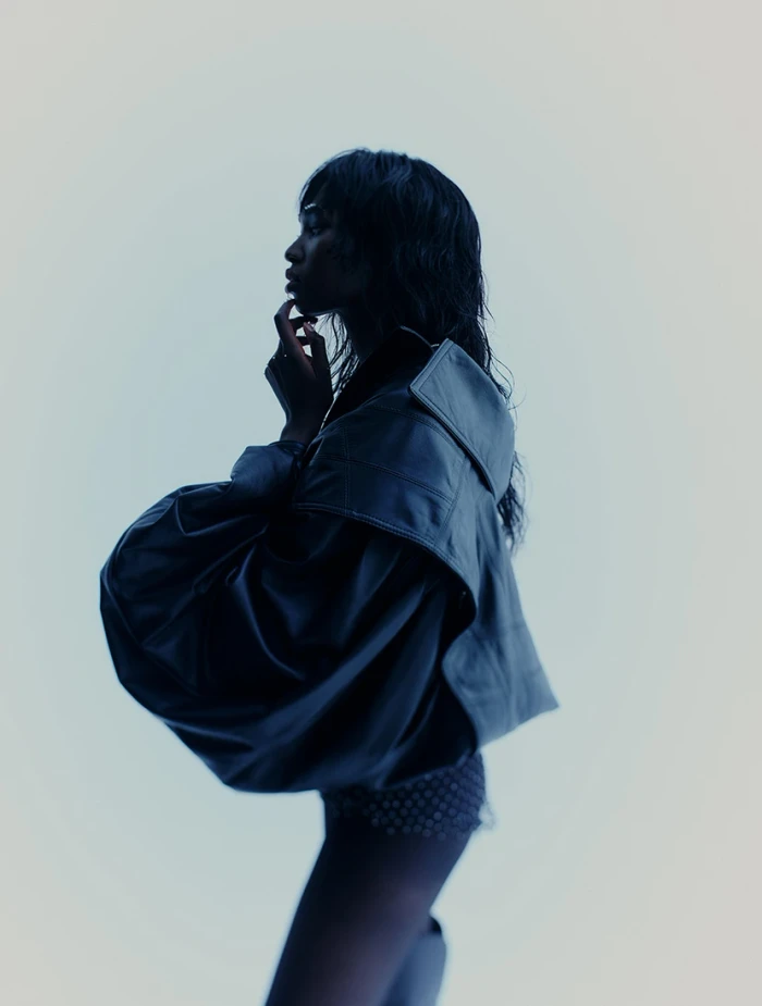 Model in silhouette wearing a dark oversized leather jacket against a light grey background