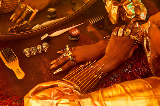 Close-up of a person's hands adorned with rings, set against a background featuring grooming tools and accessories on a wooden table.