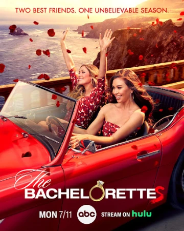 Two women riding in a red convertible driving across a coastal bridge with falling red rose petals