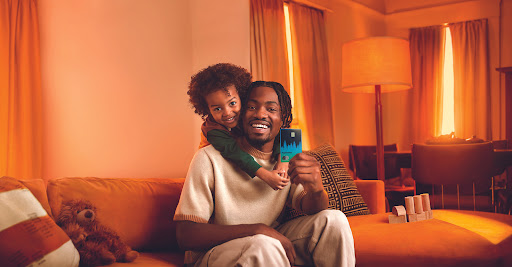 A smiling father and child pose indoors, with the father holding a credit card, creating a warm, family-focused financial image.