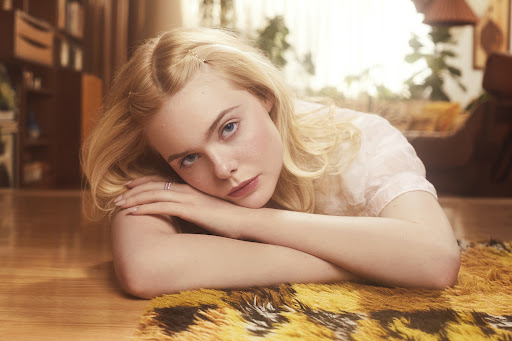 Close-up portrait of a blonde woman lying on a patterned rug, with a soft, vintage-inspired aesthetic in an indoor setting.