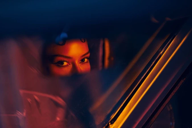 Close-up portrait of a woman framed through a car window with warm amber and magenta neon lighting by Gizelle Hernandez.