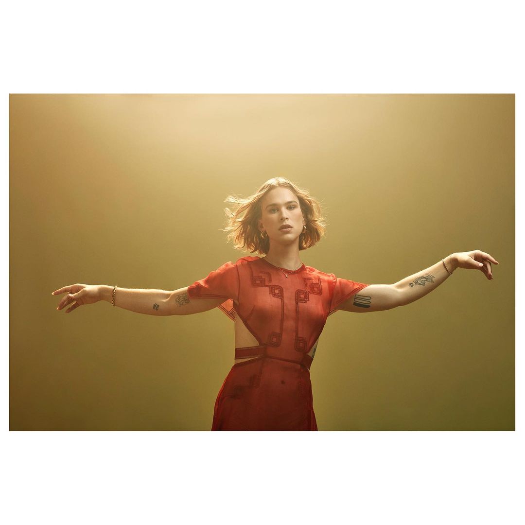 Young woman in a red dress with open arms, portrait framed with a smooth gold background and soft lighting, stylish contemporary fashion.