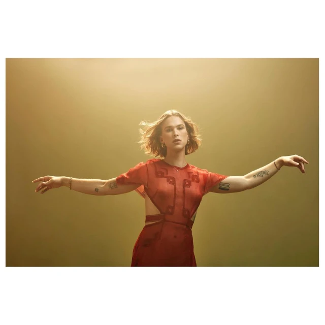 Young woman in a red dress with open arms, portrait framed with a smooth gold background and soft lighting, stylish contemporary fashion.