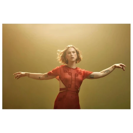 Young woman in a red dress with open arms, portrait framed with a smooth gold background and soft lighting, stylish contemporary fashion.
