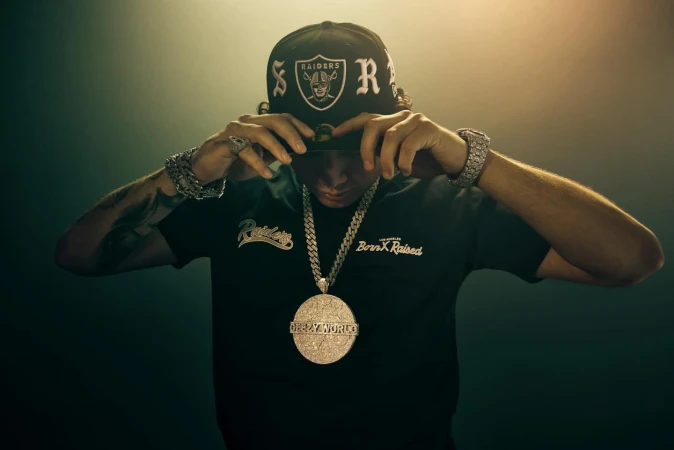 Man adjusting black cap and wearing large diamond pendant necklace and chunky bracelets by photographer Gizelle Hernandez