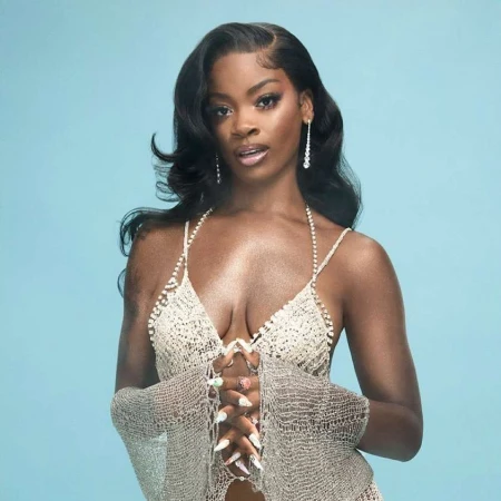 Black woman with long dark wavy hair wearing a sparkling halter top and matching sleeves against a light blue background.