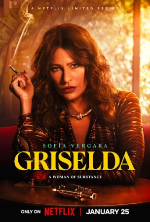 Portrait of Sofia Vergara holding a lit cigarette and sitting at a dark table with a small gun resting on the surface.