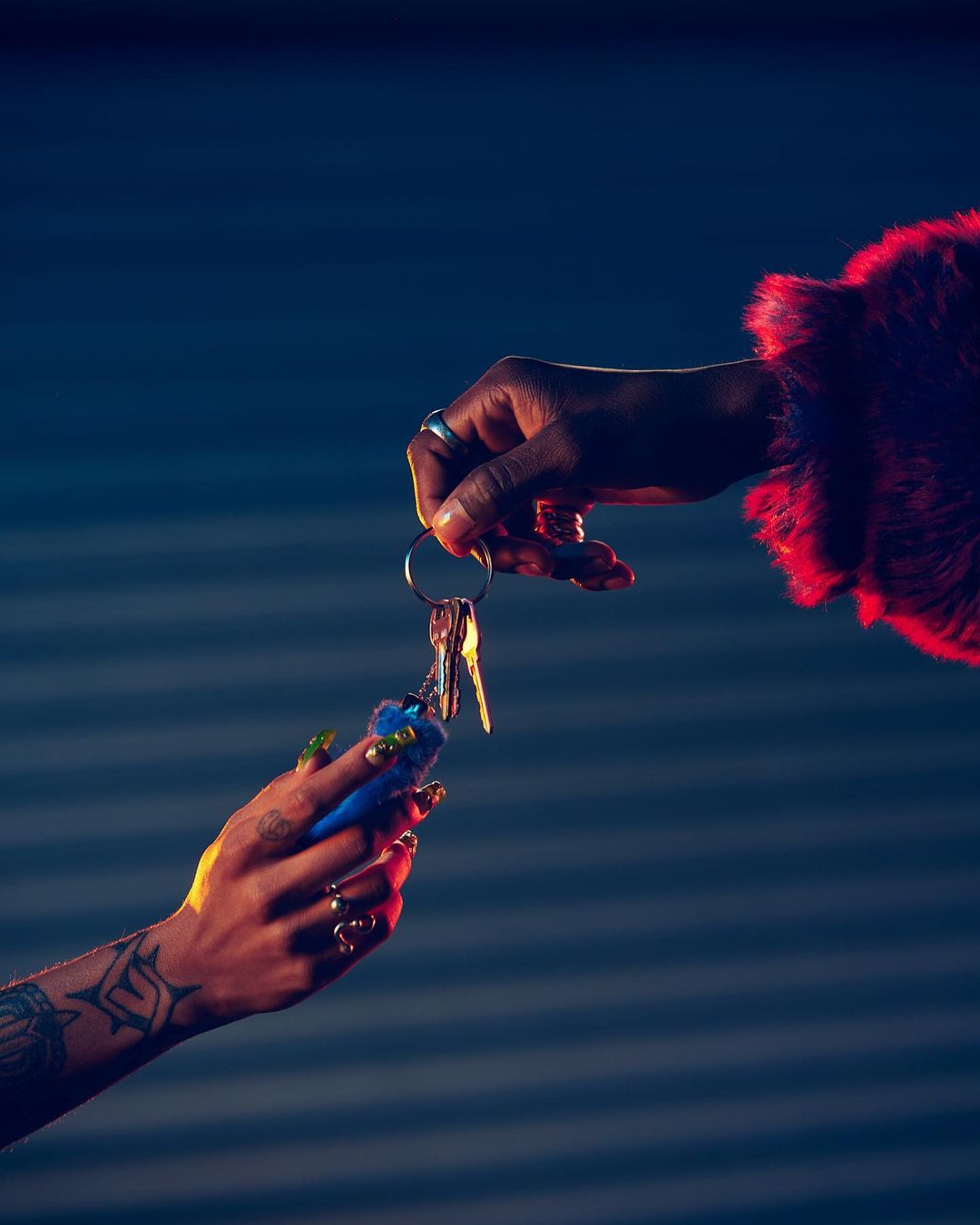 Close-up of two hands exchanging keys with a fluffy keychain against a blurred blue background with red and blue lighting.