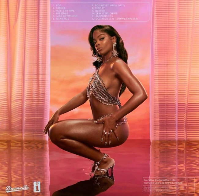 A dark-skinned woman is crouched with a glimmering metal-beaded top and bottom; a reflective surface adds depth to the image.