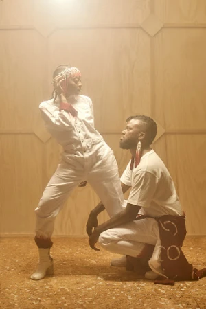 Two models in white outfits posing against a wooden paneled wall, photographed by Gizelle Hernandez.