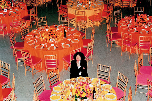 Overhead shot of woman sitting at table among banquet tables with colorful floral centerpieces, place settings, and decor in event space.