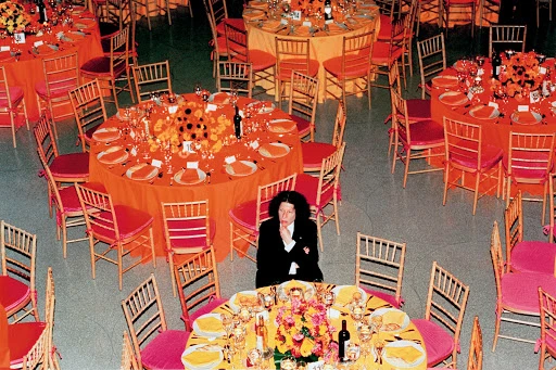 Overhead shot of woman sitting at table among banquet tables with colorful floral centerpieces, place settings, and decor in event space.