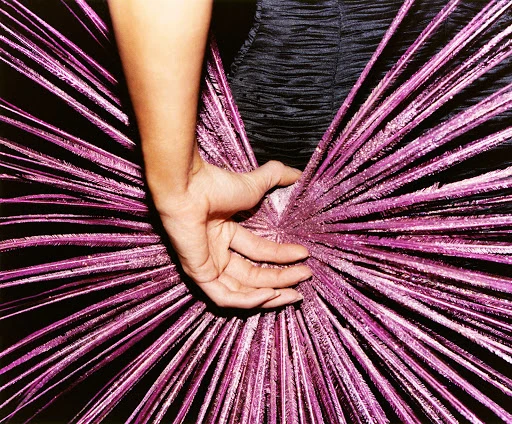 Close-up shot of a hand holding a spiky, purple starburst object with a woman in a black dress partially visible in the background.