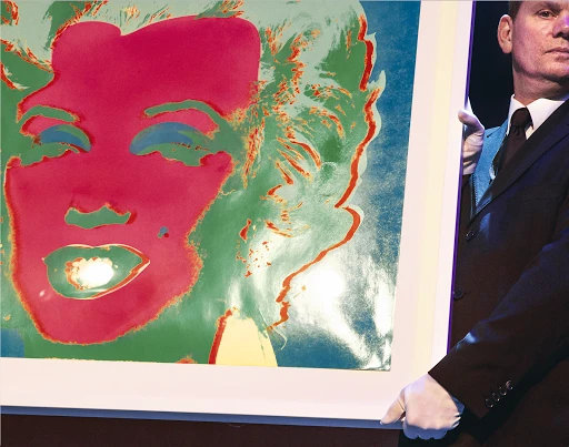 Colorful pop art print of a woman's face is held by a man in a suit and white gloves, presented in a brightly lit setting.