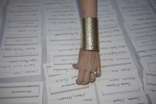 Close-up on a fair-skinned adult hand with a gold hammered cuff bracelet and ring, selecting from a stack of name cards.