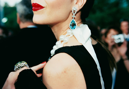 Elegant woman at a red-carpet event, showcasing a black dress, striking red lipstick, and exquisite jewelry including a large ring and earrings.