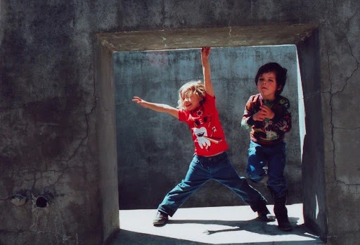 Two young children playing near a concrete structure, one hanging from the top, the other standing beside, both in casual clothes.