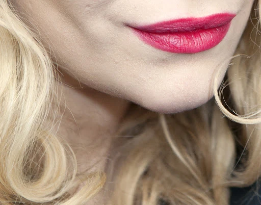 Close-up of an adult female with blonde wavy hair and red lipstick, featuring a partial view of the face focusing on the mouth and chin.