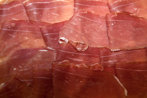Close-up of thinly sliced cured ham, featuring varying shades of pink and red with a visible fatty marbling texture.