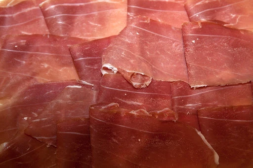 Close-up of thinly sliced cured ham, featuring varying shades of pink and red with a visible fatty marbling texture.