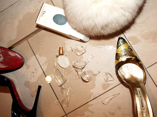 Elevated view of broken perfume bottle, luxury heels, and Dior box on a tiled floor suggesting wealth and carelessness.