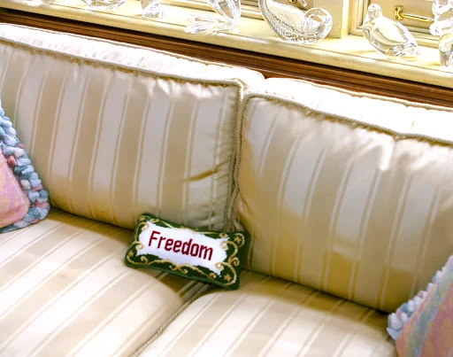 Upholstered cream striped couch with pillows, including a green pillow with the word 'Freedom' stitched in red thread.