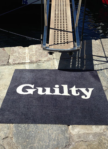 Entrance to a boat with gangway ladder leading onto a grey carpet doormat with the word 'Guilty' in white font.