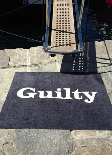 Entrance to a boat with gangway ladder leading onto a grey carpet doormat with the word 'Guilty' in white font.