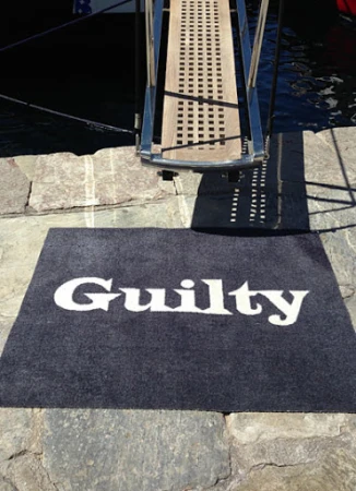 Entrance to a boat with gangway ladder leading onto a grey carpet doormat with the word 'Guilty' in white font.