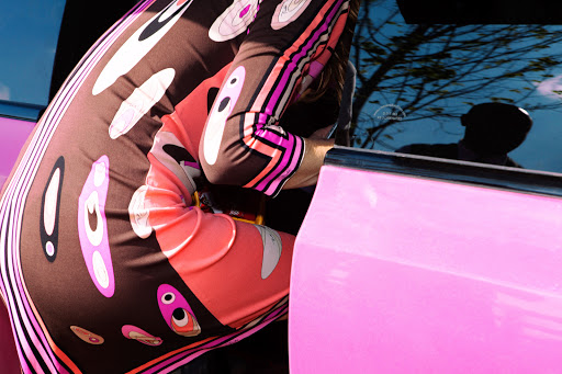 Fashion image of a woman in a patterned dress with pink car. Close-up shot highlighting her sleeve and side while she interacts with the vehicle.