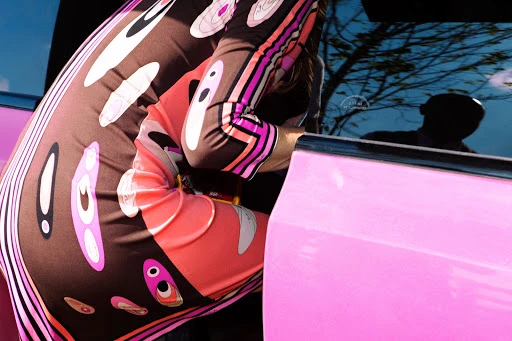 Fashion image of a woman in a patterned dress with pink car. Close-up shot highlighting her sleeve and side while she interacts with the vehicle.