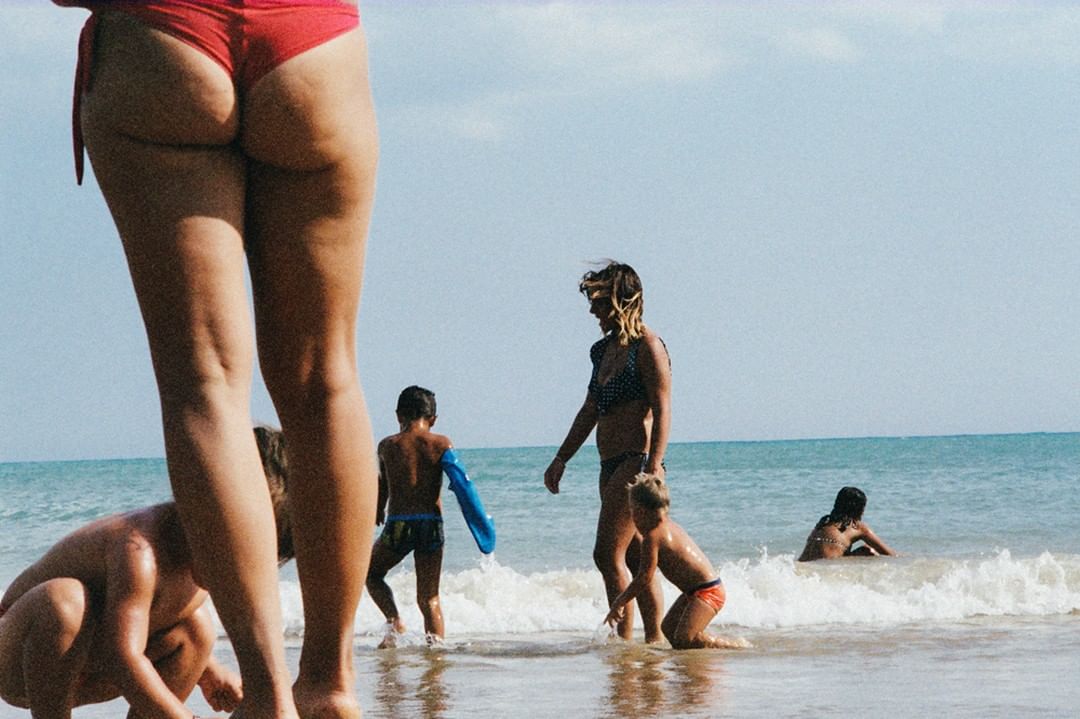 Children and a woman in swimwear enjoy the beach with blue ocean waves in the background on a sunny day. Summer beach scene.