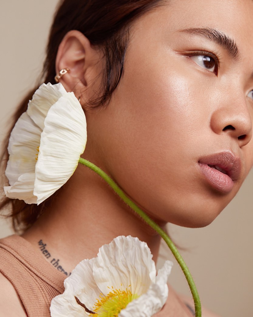 Close up portrait of a young woman holding white poppy flowers against a neutral beige background by Kayla Varley