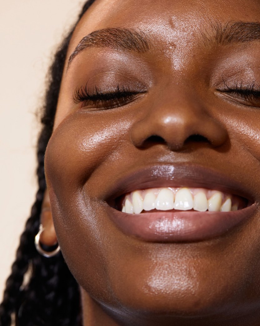 Close-up portrait of a smiling Black woman with glossy lips and glowing skin by photographer Kayla Varley