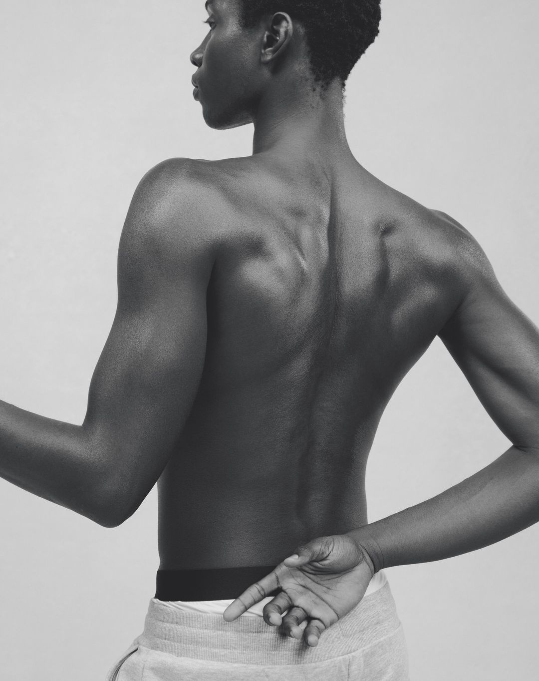Striking monochrome portrait of a bare-chested Black male model with arms crossed, showcasing muscular physique and minimalist style.