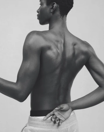 Striking monochrome portrait of a bare-chested Black male model with arms crossed, showcasing muscular physique and minimalist style.
