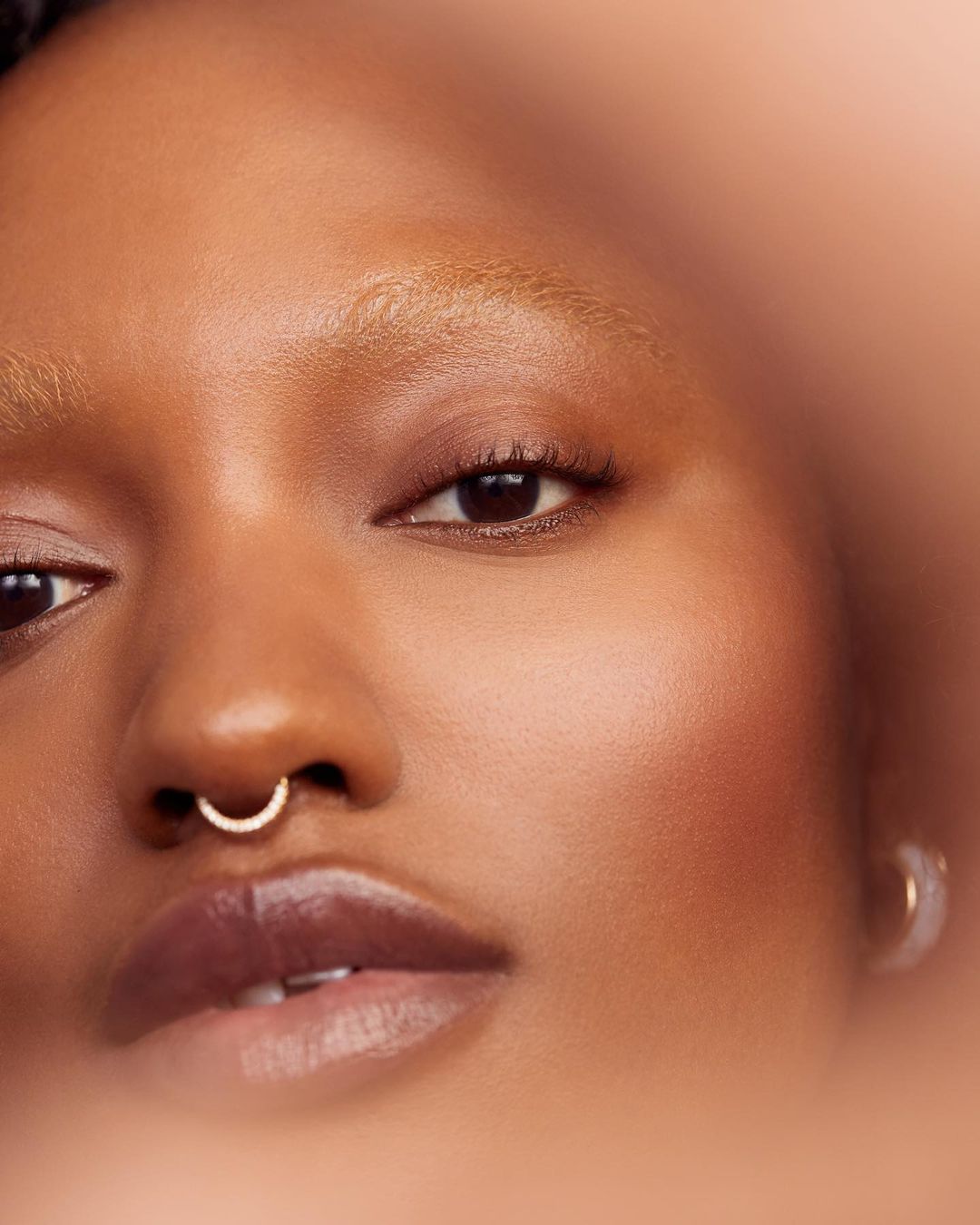 Close-up portrait of a Black woman with light brown skin, light blonde hair, and a silver nose ring, showcasing natural beauty and texture.