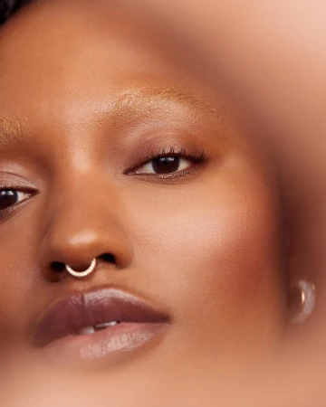Close-up portrait of a Black woman with light brown skin, light blonde hair, and a silver nose ring, showcasing natural beauty and texture.
