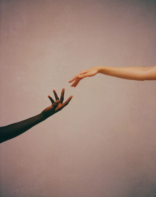 Conceptual image of two hands of different skin tones reaching out to each other against a gradient background. Interracial unity.