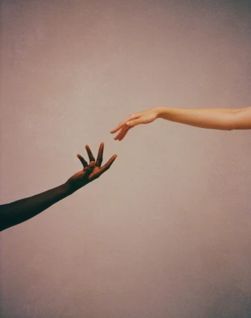Conceptual image of two hands of different skin tones reaching out to each other against a gradient background. Interracial unity.