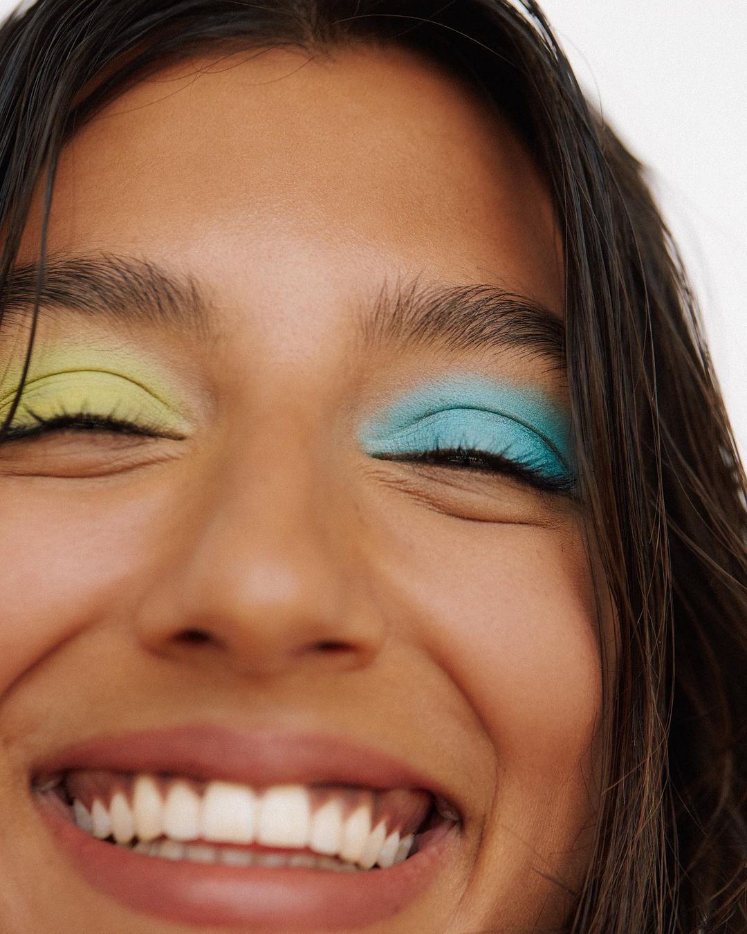 Close-up portrait of a smiling woman with bright yellow and blue eyeshadow, photographed by Kayla Varley.